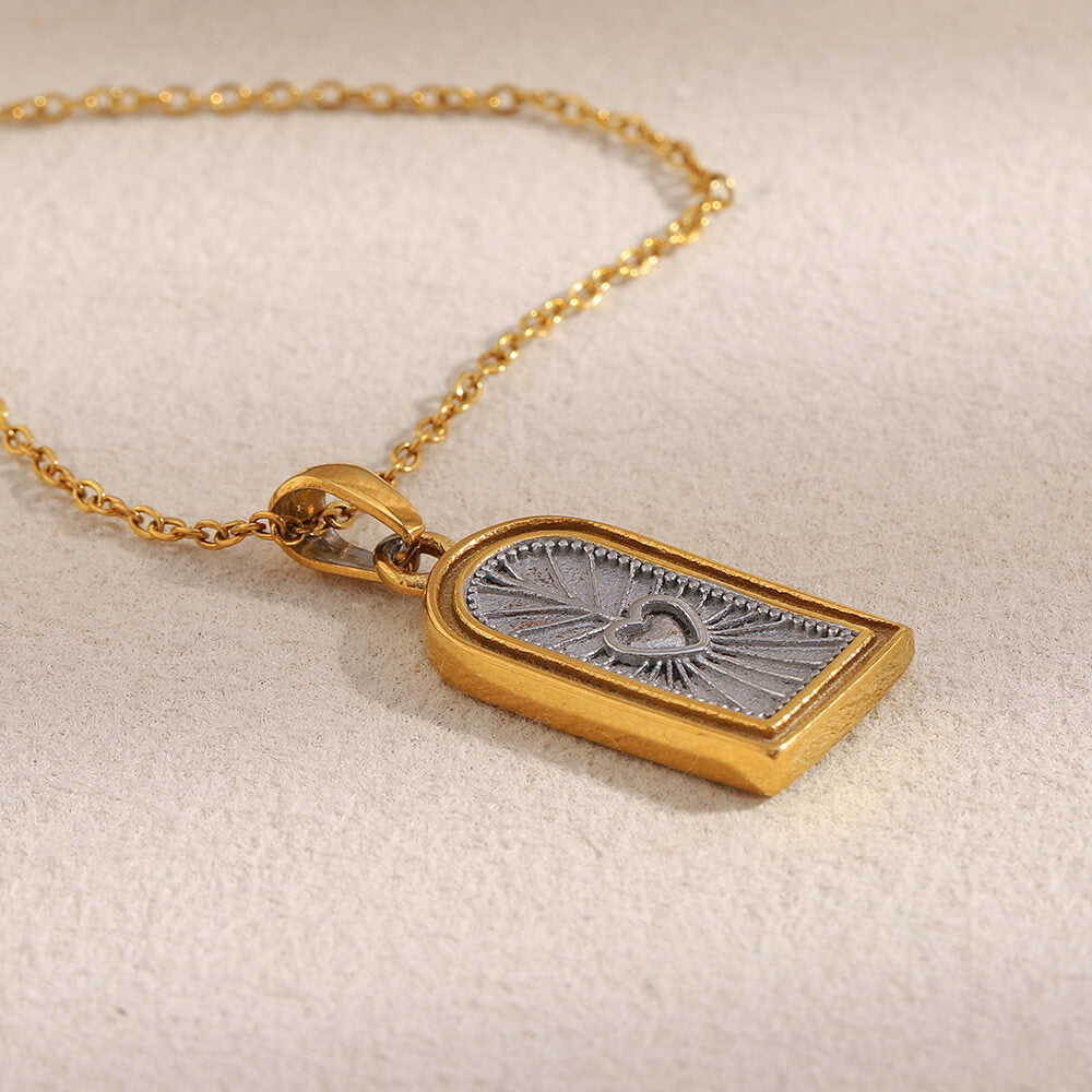 Gold necklace with a rectangular pendant on a beige background.