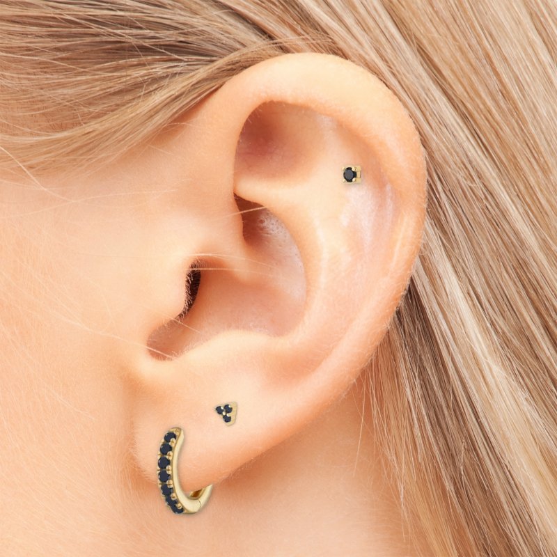 A woman wearing multiple gold earrings wtih black CZ stones.