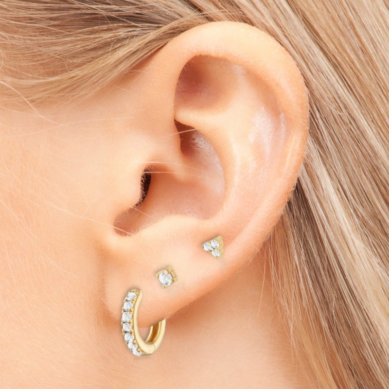 A woman wearing multiple gold earrings with clear CZ stones.