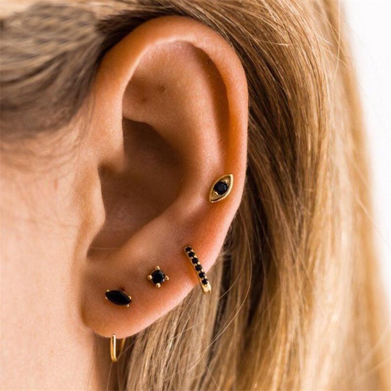 A woman wearing gold hoops and studs with black stones.