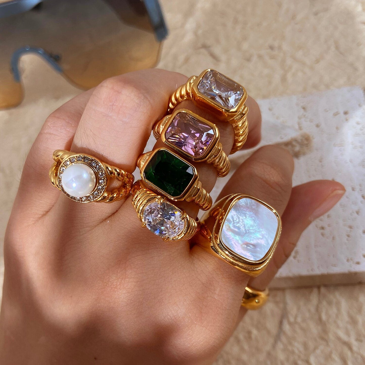 A woman wearing a bunch of chunky gold gemstone rings.