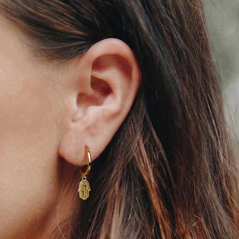 A woman modeling the Hamsa Hand CZ Huggies in gold.