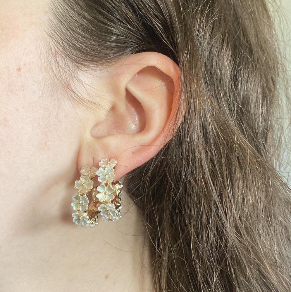 A model wearing Iridescent Flower Hoops in Gold.