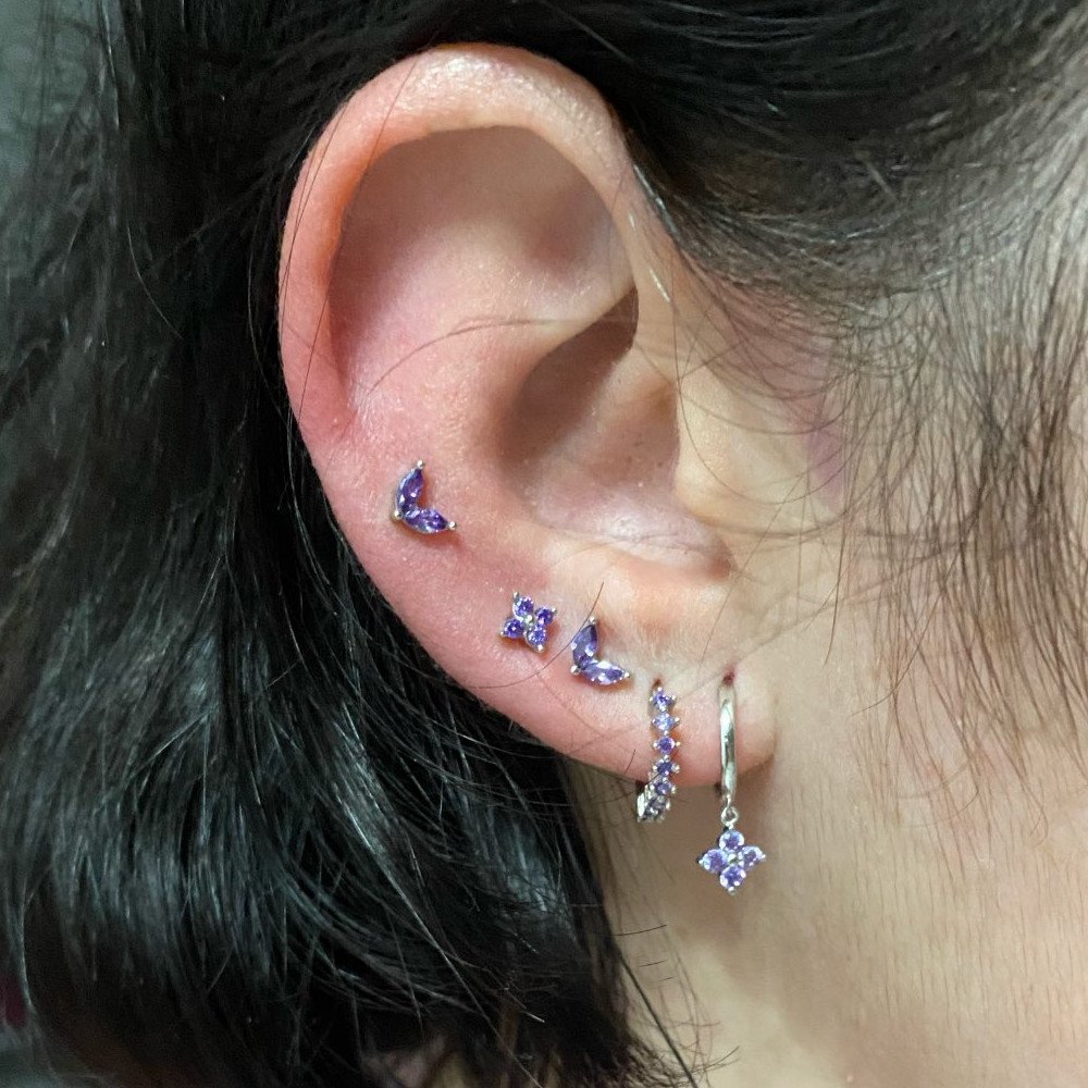 A woman wearing multiple silver earrings with purple CZ stones.