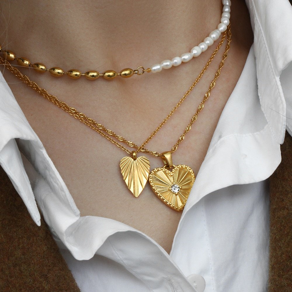 A model wearing multiple gold heart necklaces.