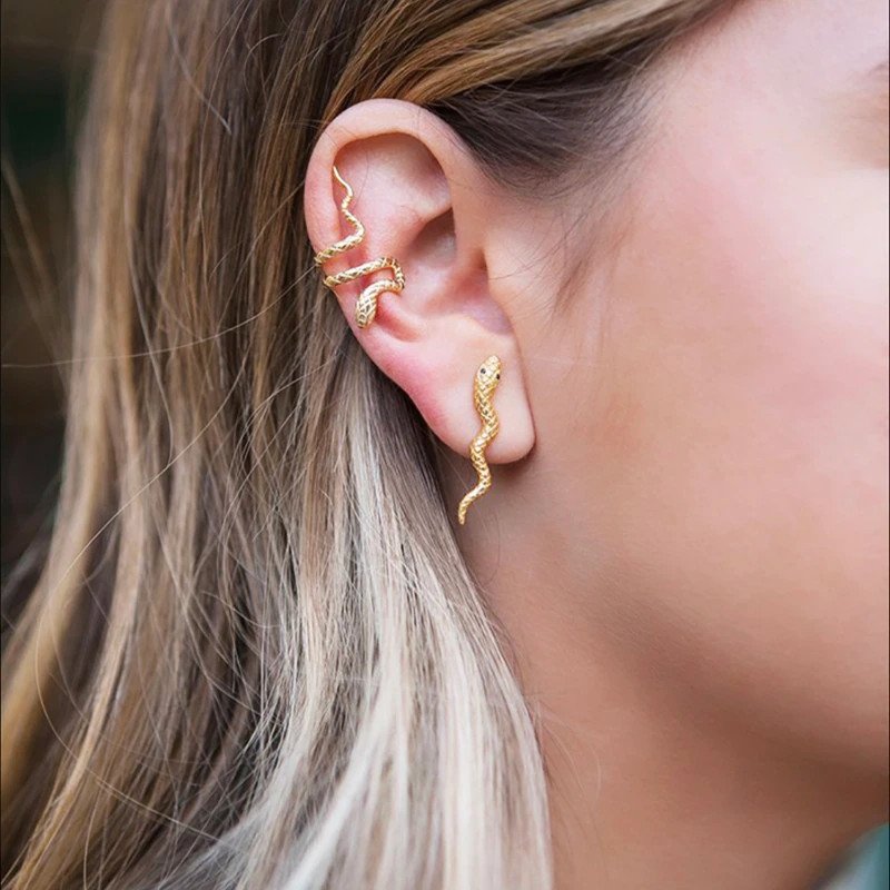 A woman wearing gold snake earrings.
