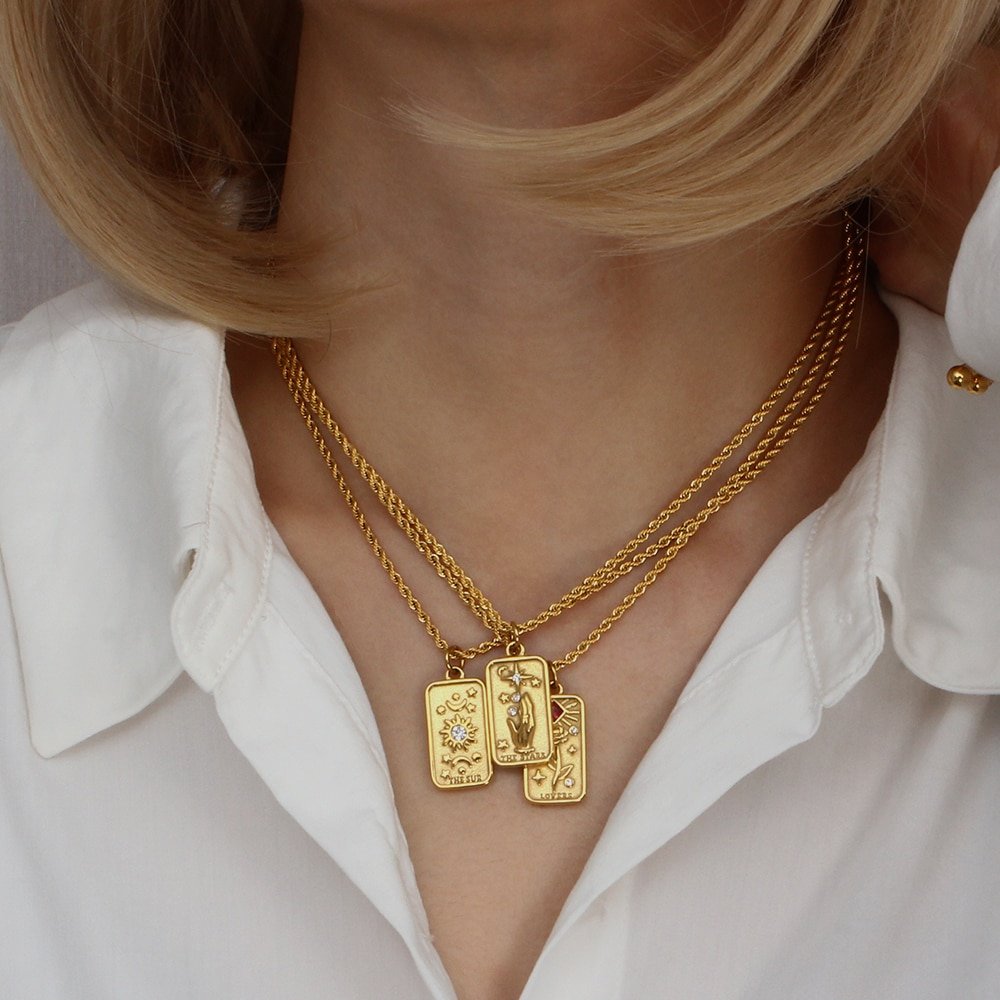 A model wearing gold tarot card necklaces with gemstones.