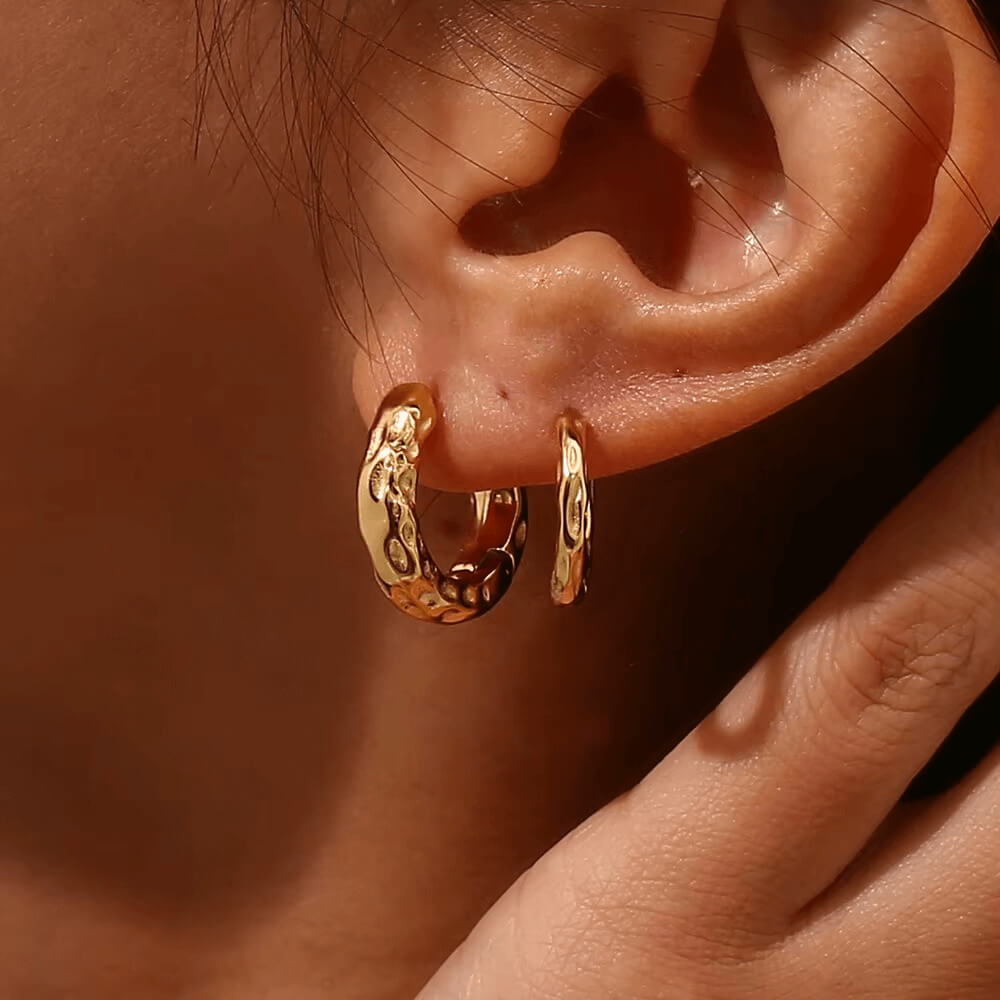 Close-up of an ear wearing gold hoop earrings with a blurred background.