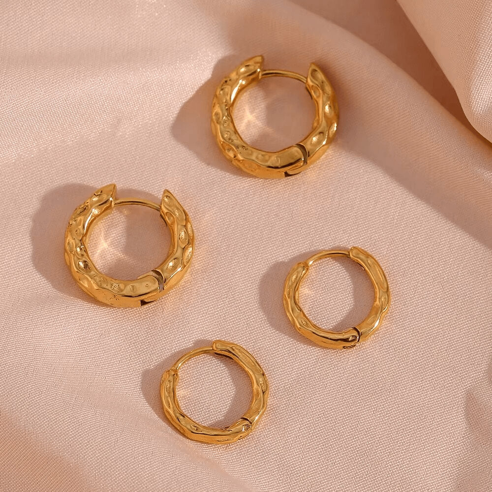 Set of gold hoop earrings on a beige fabric background.