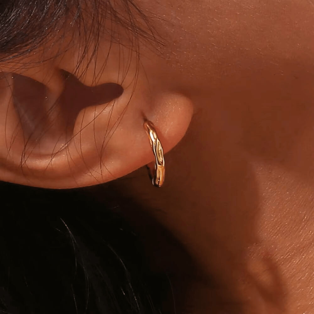 Gold hoop earring worn by a person with dark hair and skin.