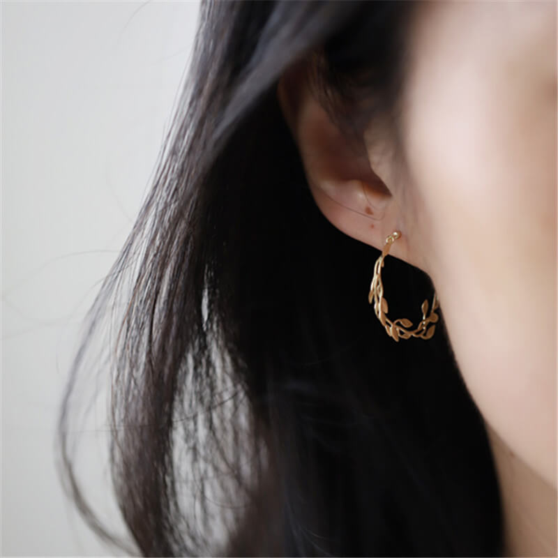 A woman wearing leave branch hoop earrings.