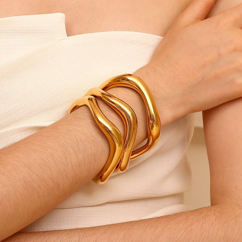 A woman wearing three gold organic bangles.