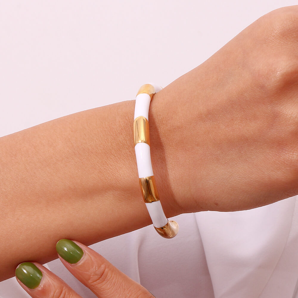 A woman wearing a gold and white enamel bangle bracelet.