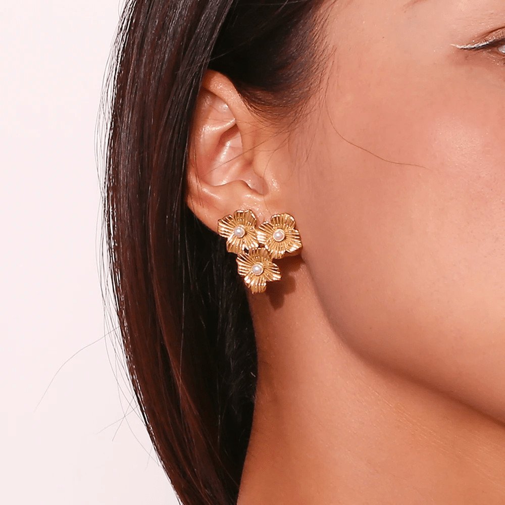 A woman wearing gold flower earrings.