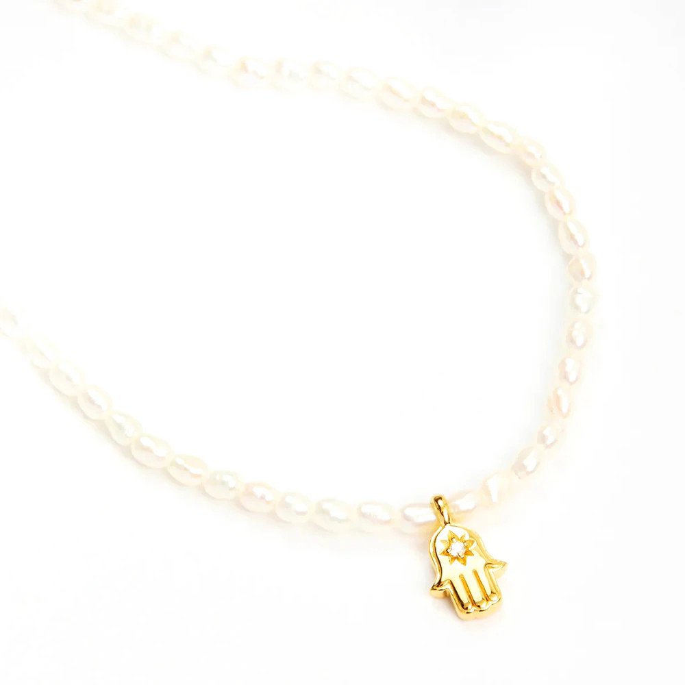 Gold hamsa hand pendant on a pearl necklace.