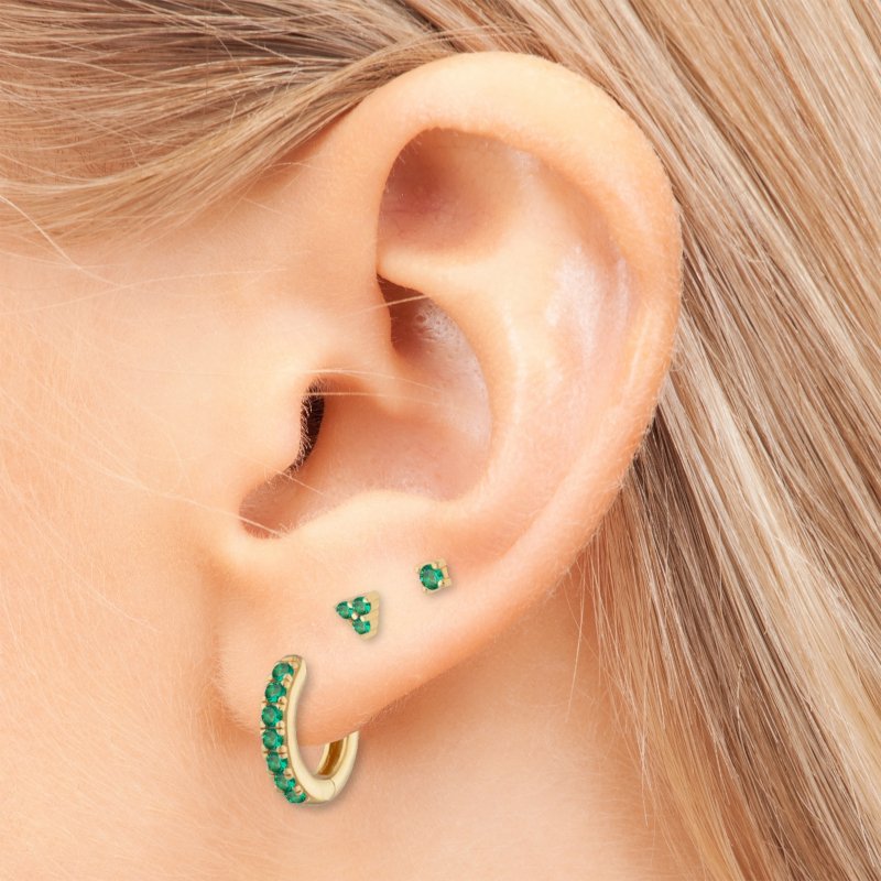 A woman wearing gold earrings with green CZ stones.