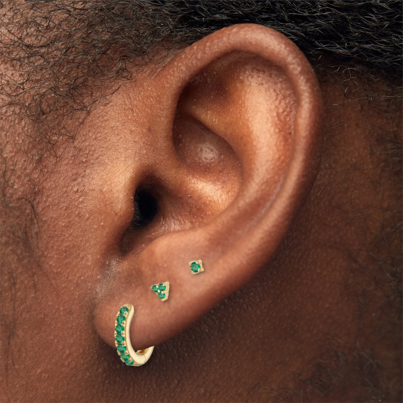 A model wearing gold earrings with green CZ stones.