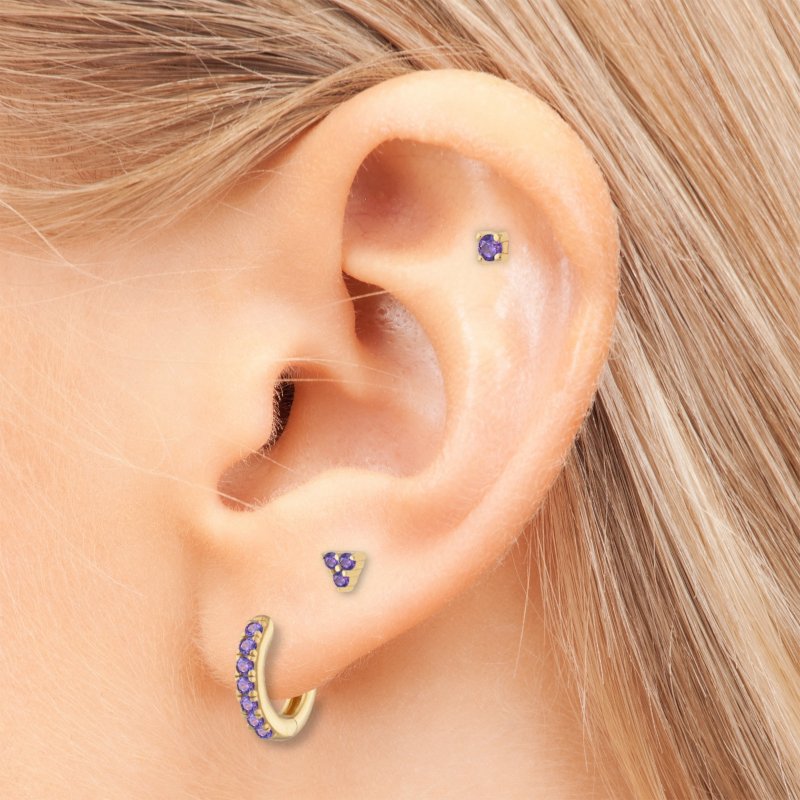 A woman wearing gold earrings with purple CZ stones.
