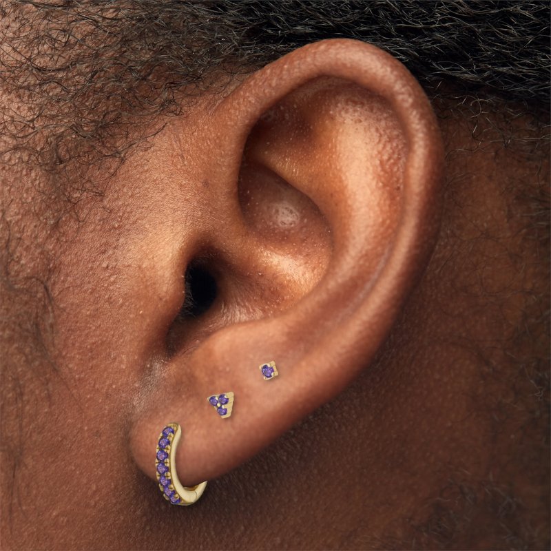 A model wearing gold earrings with purple CZ stones.