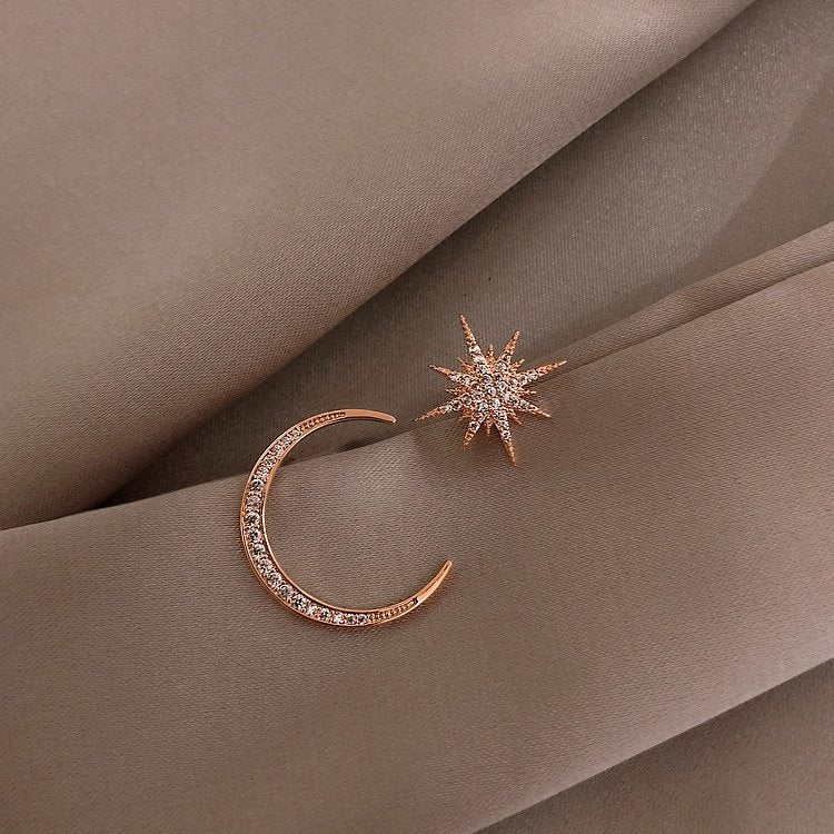 Asymmetrical Star Moon Earrings in gold on a tan fabric.