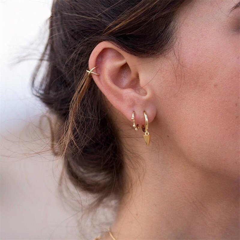 A woman wearing multiple gold mini hoop earrings.