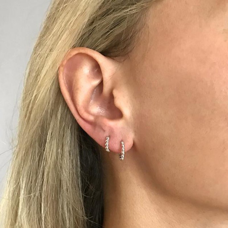 A model wearing two silver beaded huggie hoop earrings.