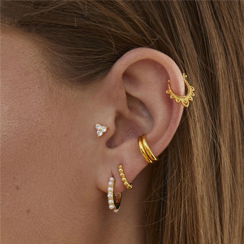 A woman wearing multiple gold and pearl hoops and ear cuffs.
