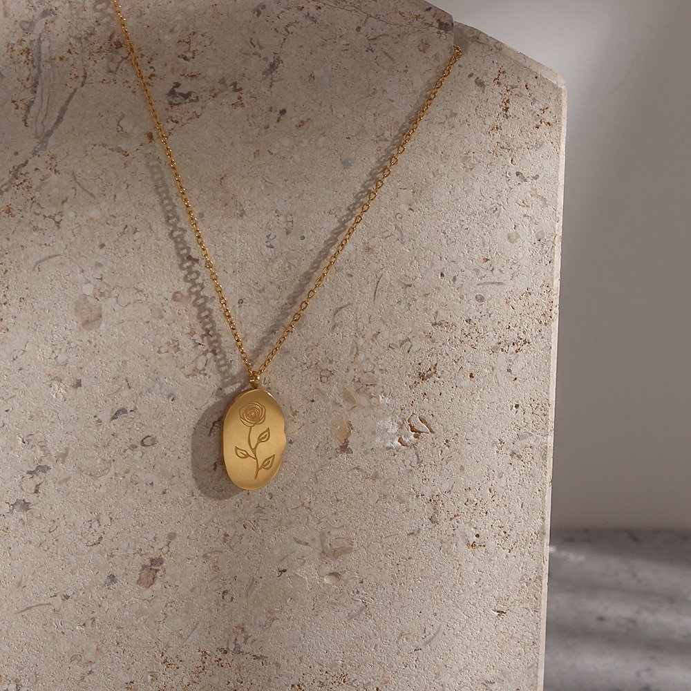 A gold pendant necklaces with an engraved birth flower.