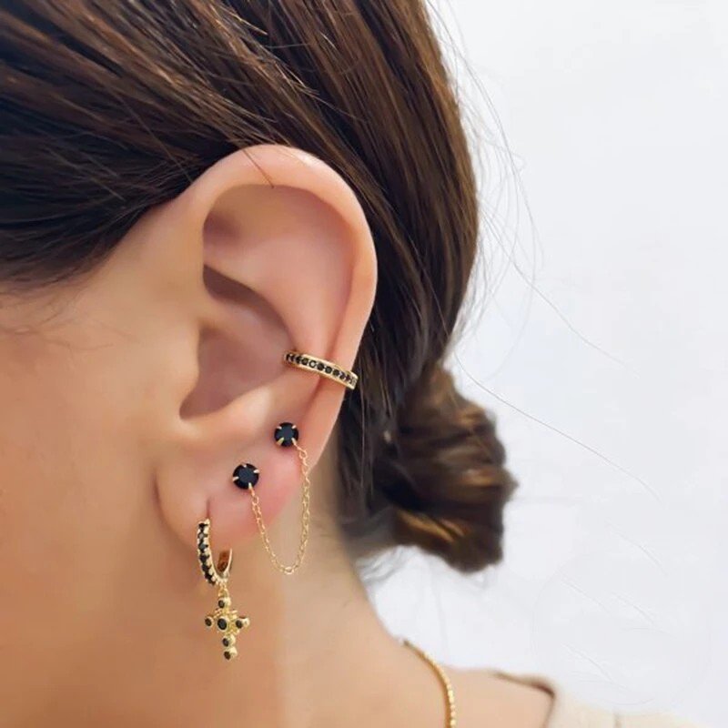A woman modeling a cross hoop, double stud chain earring and ear cuff with black stones.