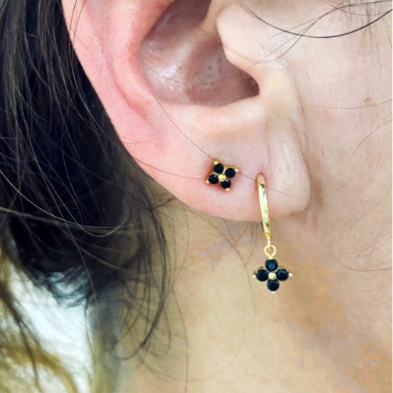 A woman wearing two black CZ gold flower earrings.