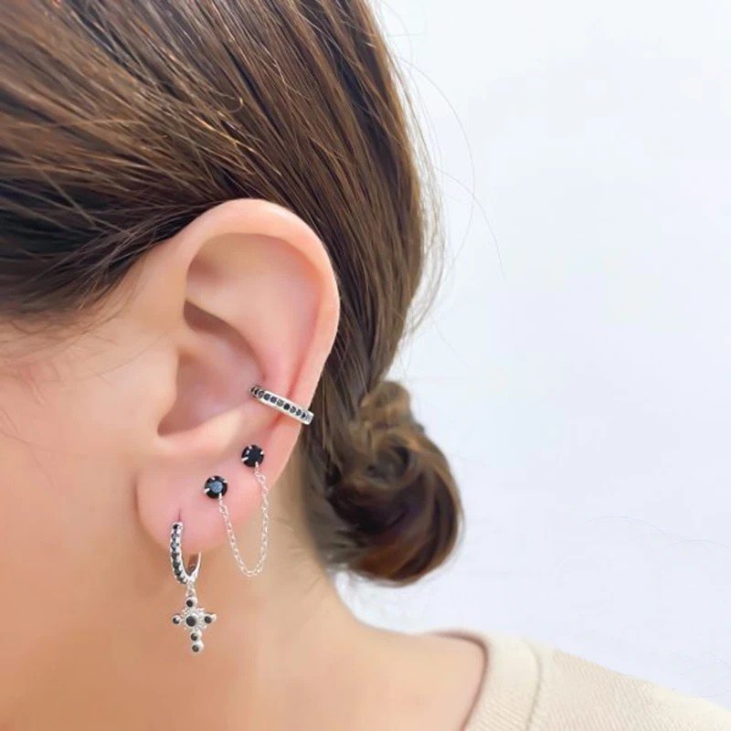 A woman wearing multiple silver earrings with black stones.