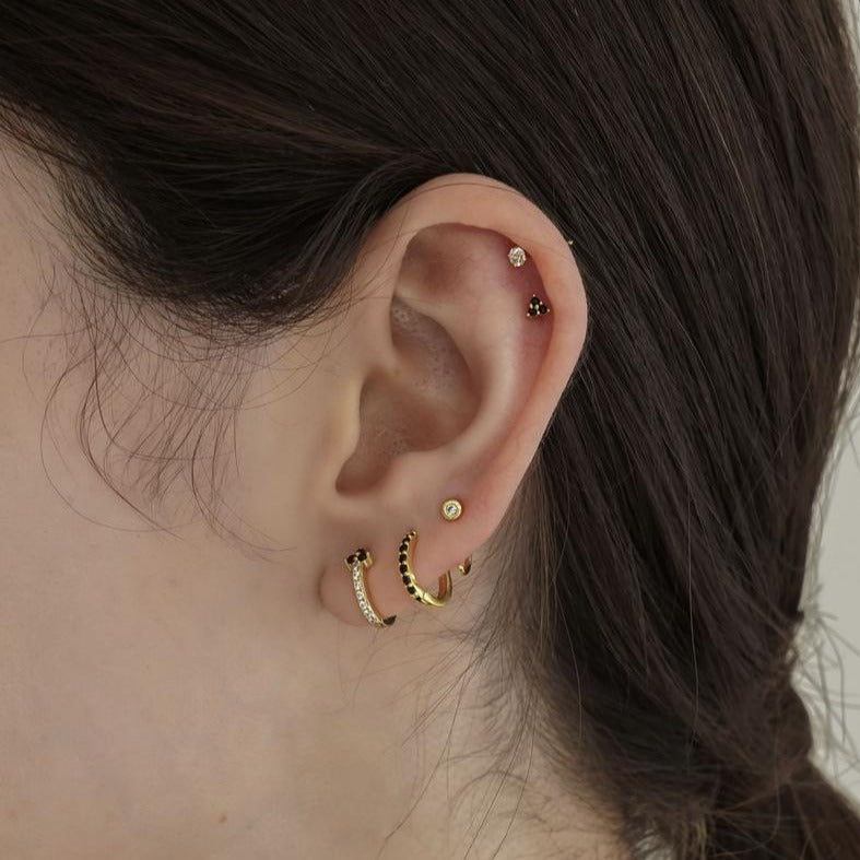 A woman modeling gold hoops and studs with black and clear CZ stones.