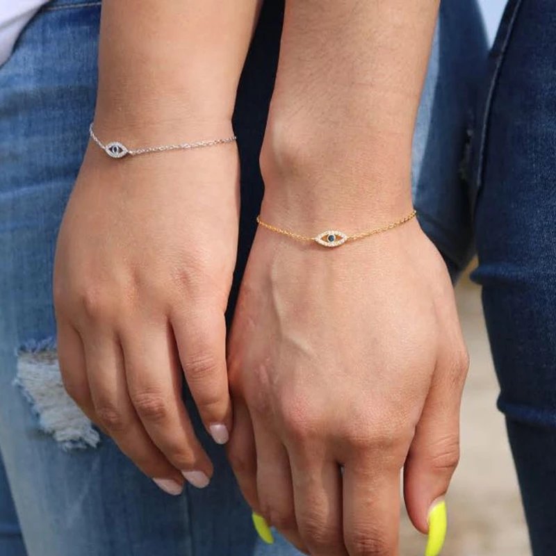 Two models wearing a gold and platinum evil eye chain bracelets.