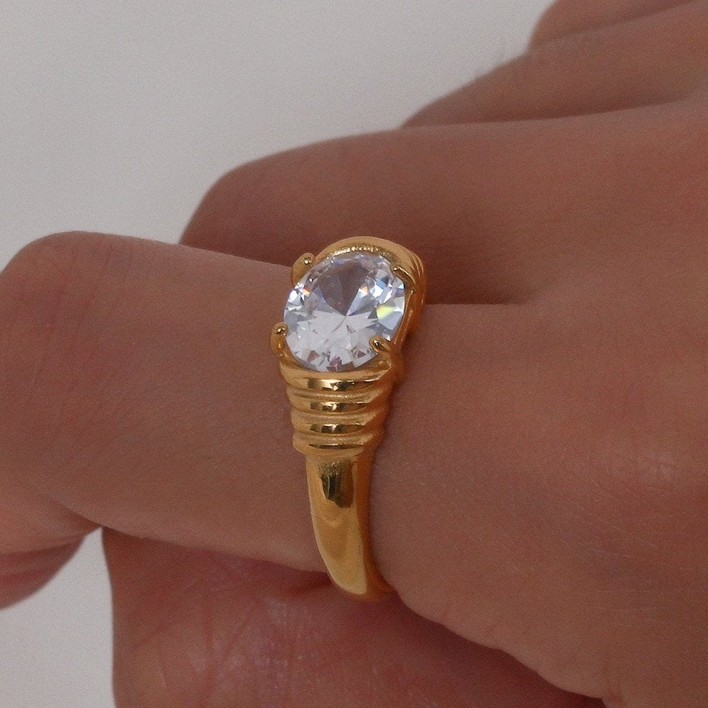 A model wearing a gold ring with clear gemstone.