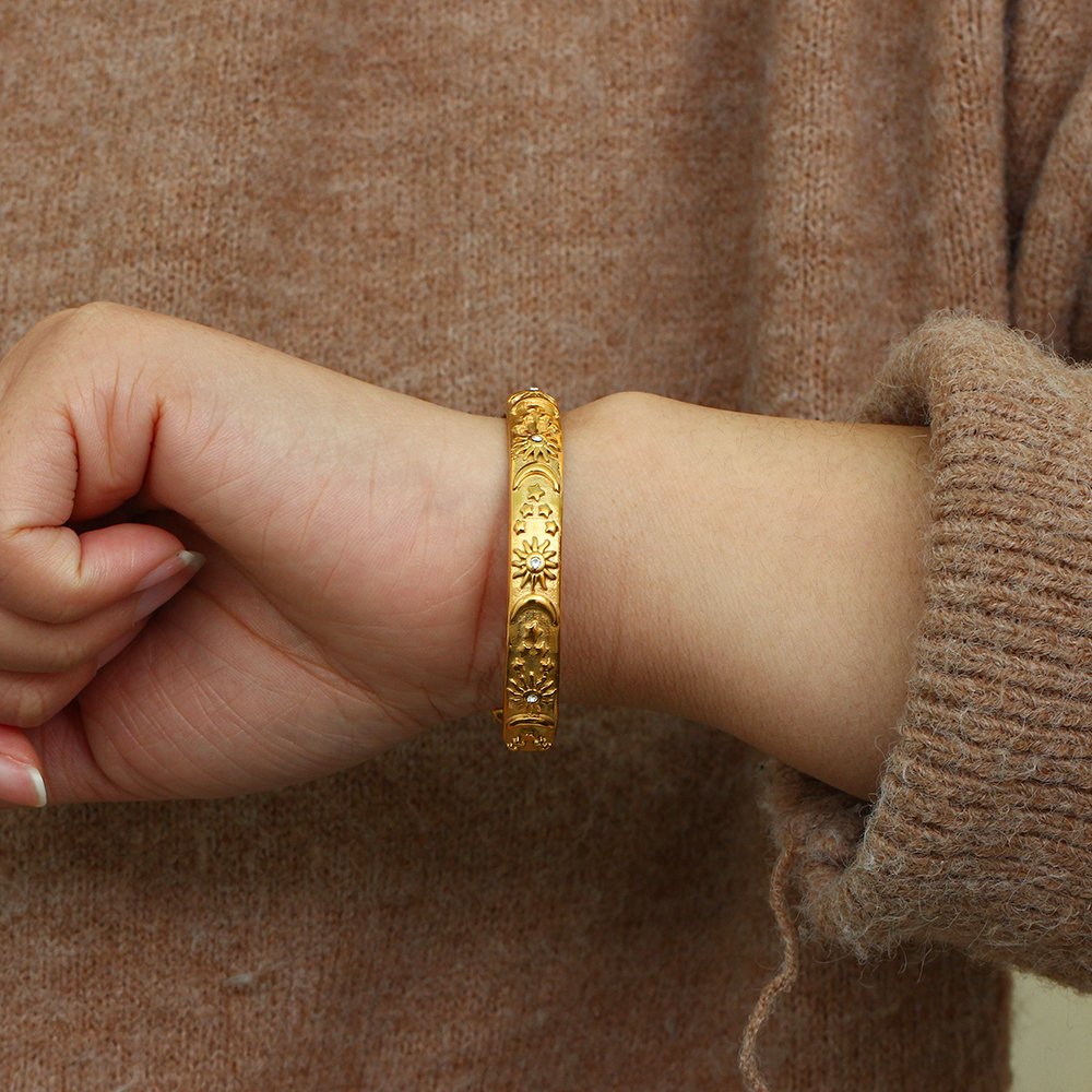 A woman wearing a gold bangle with moons and suns.
