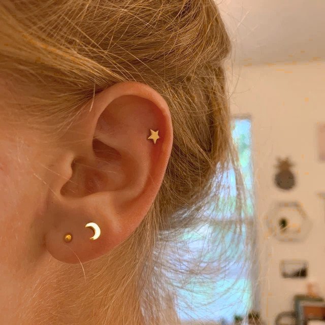 A woman wearing tiny gold moon and star stud earrings.