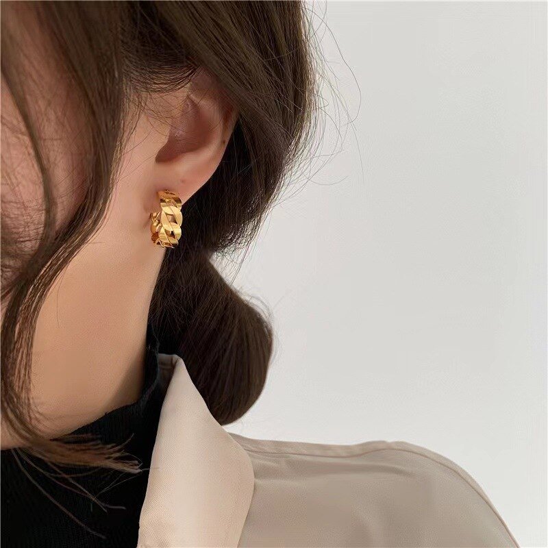A woman wearing gold chain link hoop earrings.