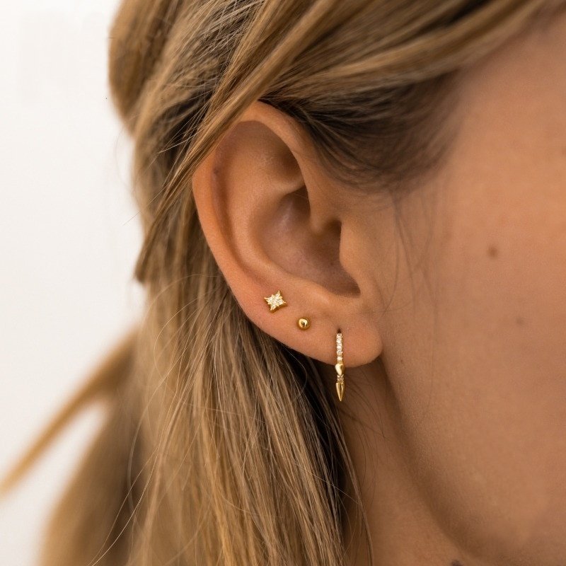 A model wearing tiny gold stud earrings.