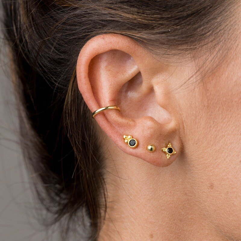 A model wearing multiple gold studs with black stones.