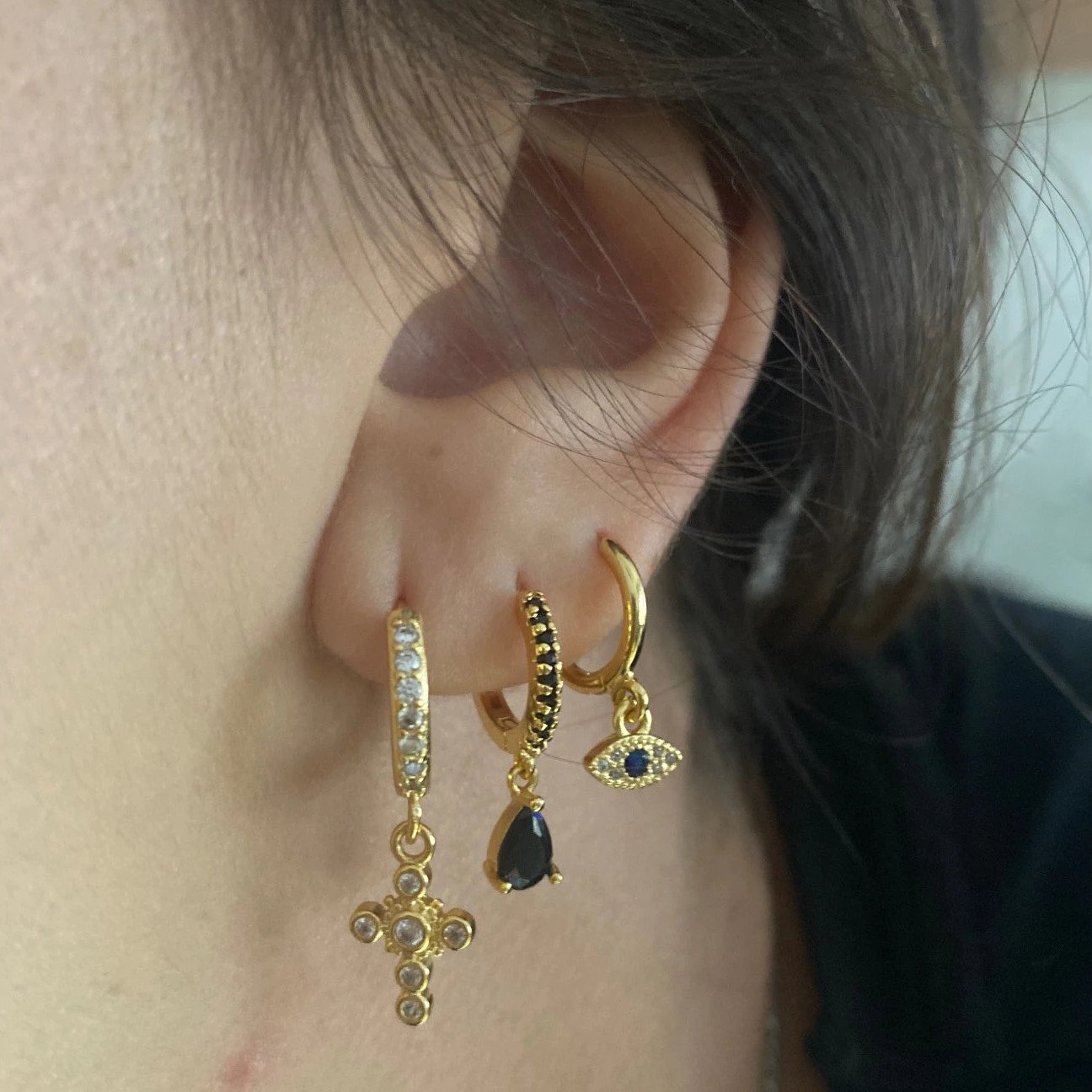 A woman wearing huggie hoop earrings with charms,