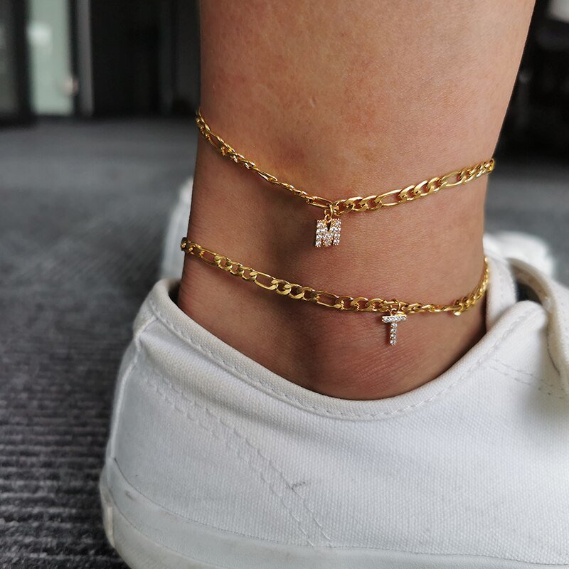 A model wearing two Crystal Initial Anklets in gold.