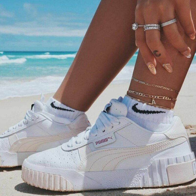 A woman wearing a gold anklets with sneakers.