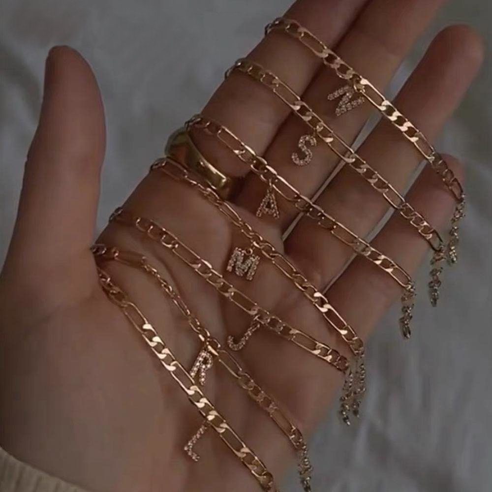 A woman holding a bunch of gold crystal initial anklets.