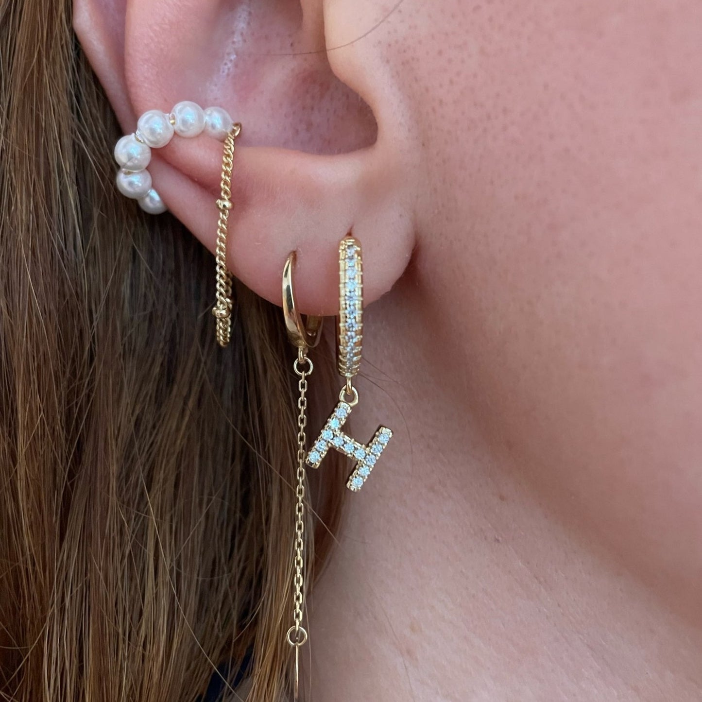 A woman wearing multiple gold initial earrings.