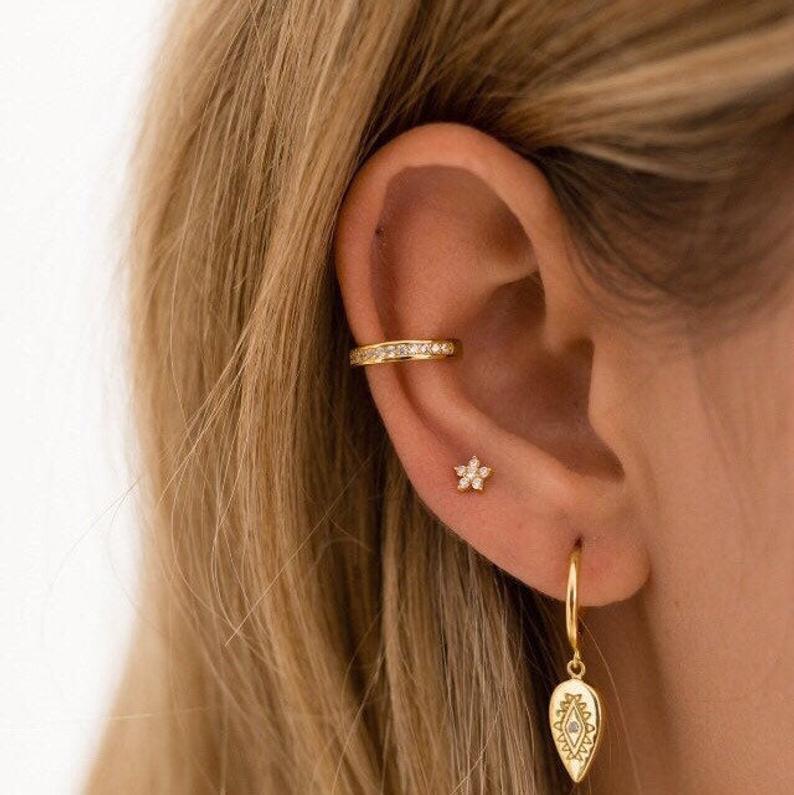 A model wearing gold hoops, studs and ear cuffs.