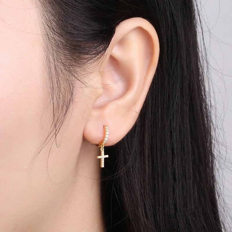 A model wearing gold cross dangle earrings.