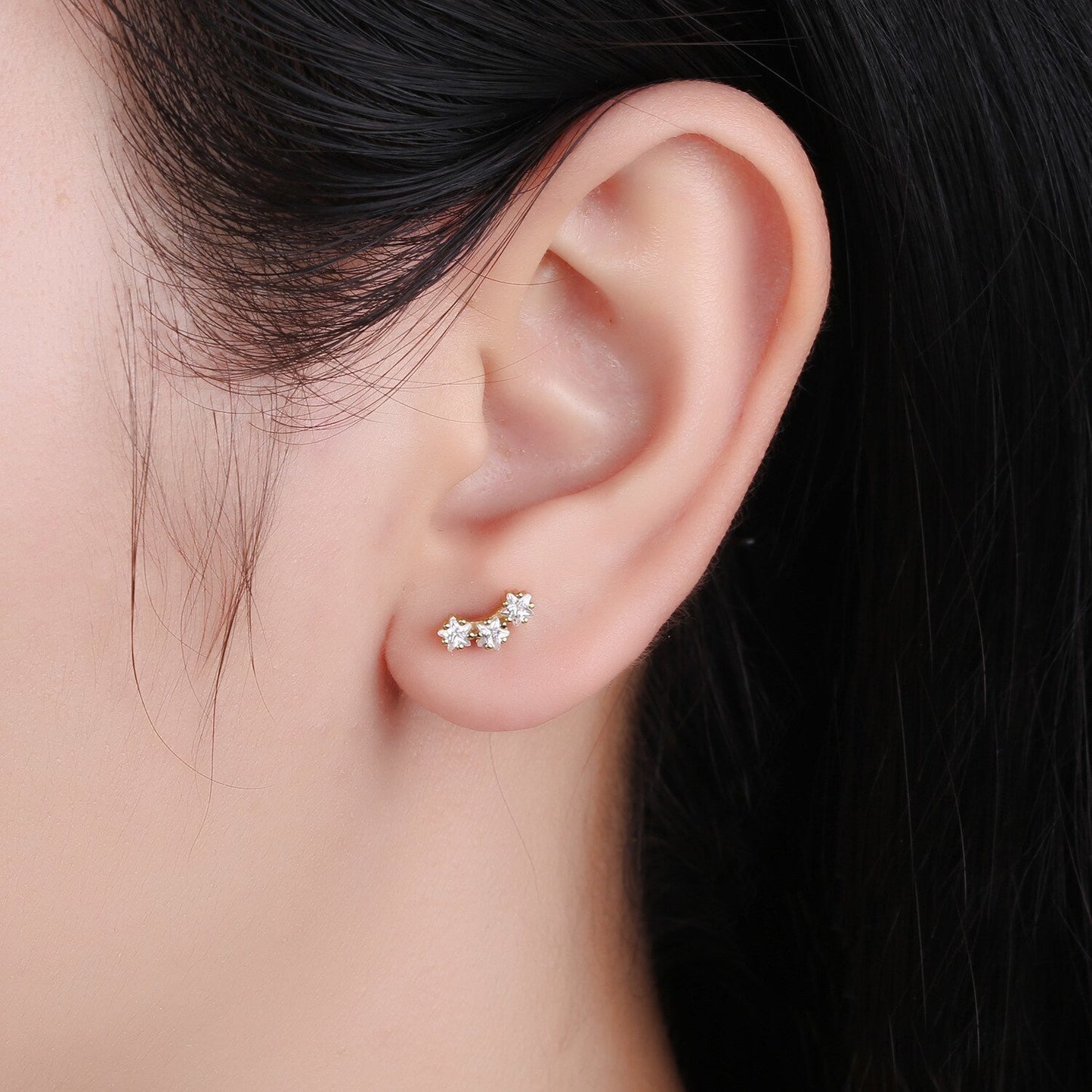 A woman wearing the gold CZ Stars Curved Studs.