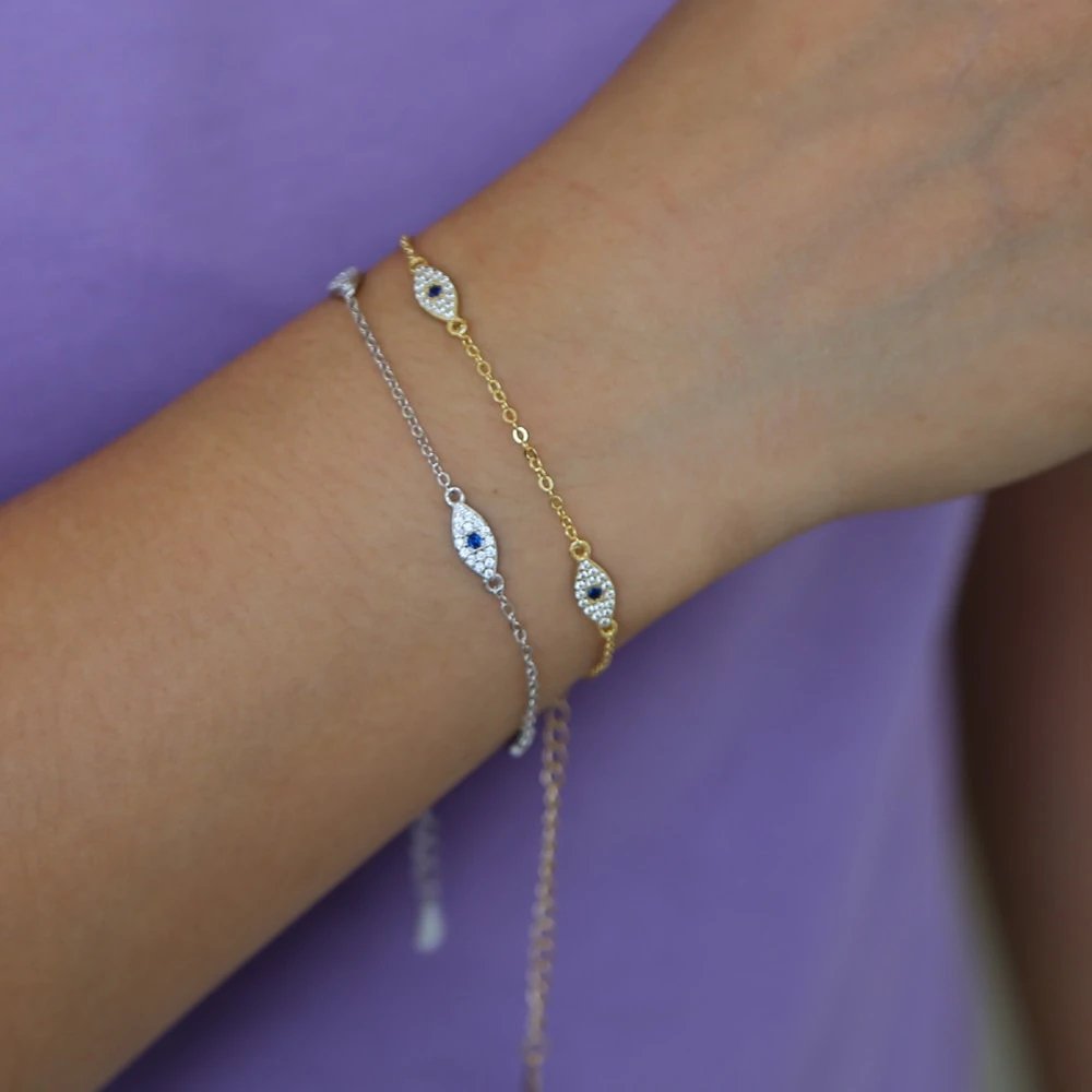 A model wearing two chain bracelets with evil eye charms in silver and gold.