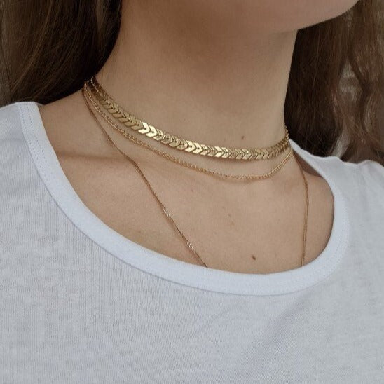 A woman wearing a gold herringbone choker necklace.