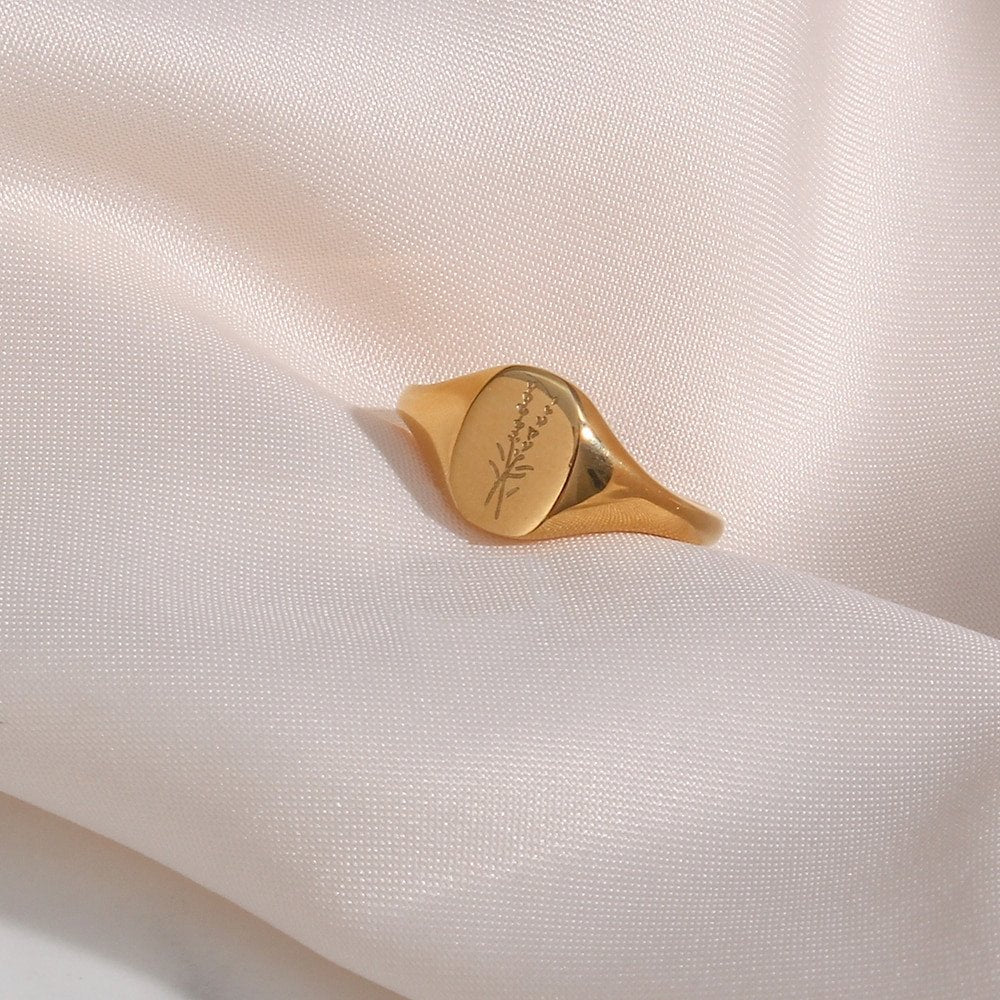 A gold oval signet ring with lavender engraving.